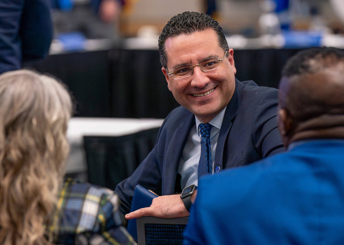 Dean Kessentini smiles while seated at a table during a meeting or conference.